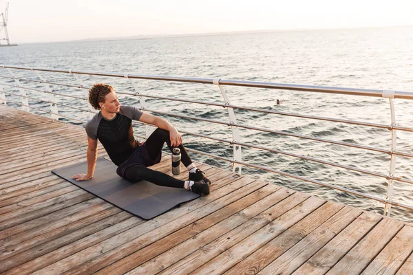 Ritratto Bellissimo Sportivo Seduto Tappeto Fitness Sulla Spiaggia Che Ascolta — Foto Stock