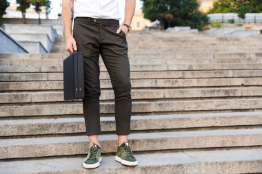 İş adamı kol cebinde duran merdivenlerde açık havada tutan evrak çantası ile kırpılmış görüntü