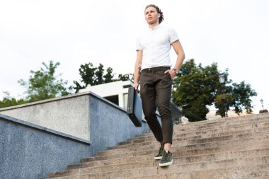 Sakin kıvırcık iş adamı kol cebinde merdivenlerde yürürken tutan evrak çantası ile tam boy görüntü