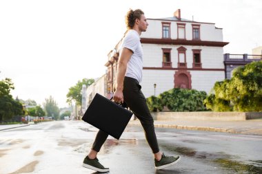 Yakışıklı kıvırcık iş adamı sokakta yürürken evrak çantası ile yan görünüm