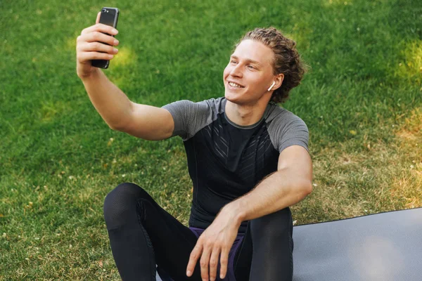 Jovem Desportista Sorrindo Ouvindo Música Com Fones Ouvido Enquanto Sentado — Fotografia de Stock