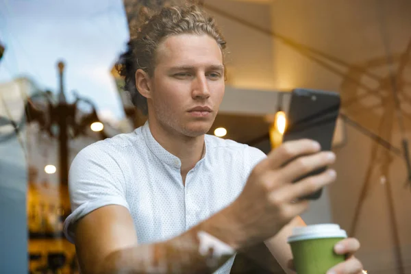 スマート フォンを使用して コーヒーを飲みながらカフェでテーブルに座っている深刻な巻き毛ビジネスマン — ストック写真