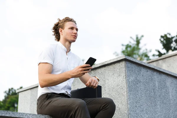 Grave Uomo Affari Riccio Con Valigetta Holdin Smartphone Guardando Lontano — Foto Stock