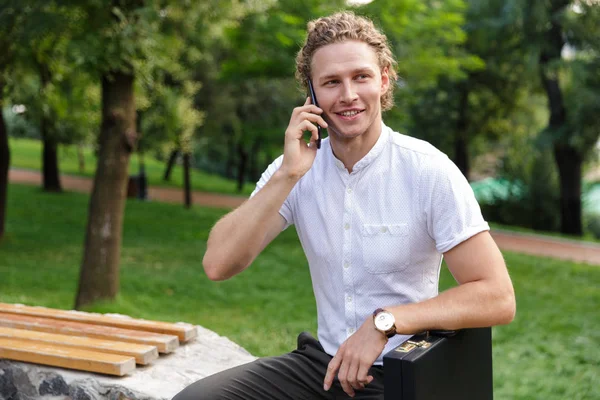 Neşeli Kıvırcık Adamı Ile Smartphone Ile Konuşmak Uzak Parkta Bankta — Stok fotoğraf