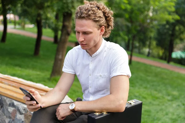 Grave Uomo Affari Riccio Con Valigetta Utilizzando Smartphone Mentre Seduto — Foto Stock