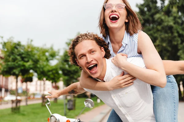 欢快的年轻夫妇一起玩滑板车 看着相机 而在公园 — 图库照片
