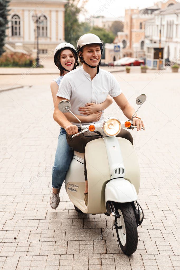 Portrait of a happy young couple in helmets riding on a motorbike together at the city street