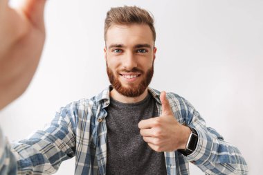 Neşeli bir genç sakallı adam üzerinde beyaz izole ayakta portresi, gösterilen bir selfie alarak thumbs up