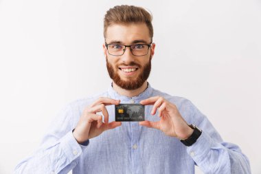 Plastik kart gösterilen bir kendine güvenen genç sakallı adam beyaz üzerinde izole ayakta gözlük portresi