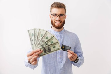 Para banknot ve kredi kartı gösteren beyaz üzerinde izole bir kendine güvenen genç sakallı adam ayakta portresi