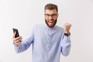 Cep telefonu, tutan bir gülümseyen Genç sakallı adam beyaz üzerinde izole ayakta gözlük portresi kutluyor