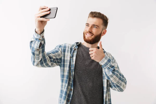 白で孤立した立っている陽気な若いひげを生やした男の肖像 Selfie を取って親指します — ストック写真