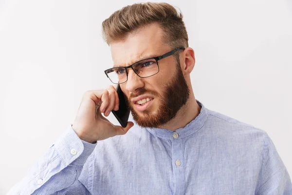 一个愤怒的年轻胡子男子的肖像站在白色的孤立 谈论手机 — 图库照片