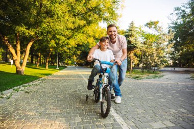 Baba ve oğlu yeşil parkta birlikte eğleniyor oğlu bisiklet kullanmayı öğretmek sevgi dolu