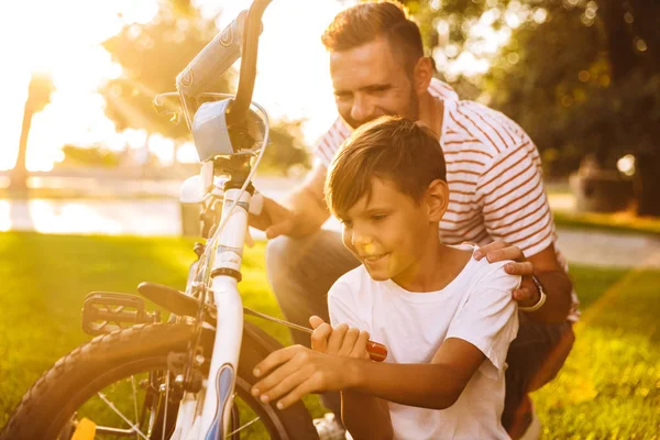 Sonriente Padre Hijo Divirtiéndose Juntos Parque Verde Arreglando Bicicleta Juntos — Foto de Stock