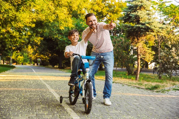 Mutlu baba ve oğlu, Bisiklet kullanmayı öğretmek yeşil parkta birlikte, eğleniyor oğlu parmak işaret