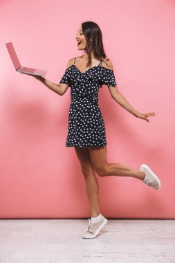 Tipik dizüstü bilgisayar kullanarak pembe arka plan üzerinde izole mutlu güzel kadın fotoğrafı.
