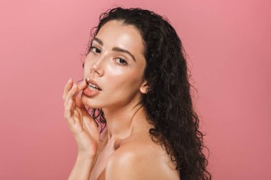 Kıvırcık esmer saçlı pembe arka plan üzerinde poz şehvetli genç bir üstsüz kadın güzellik portresi