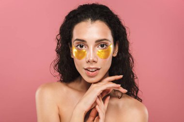 Beauty portrait of a healthy young topless woman with curly brunette hair posing over pink background, wearing cosmetic eye patches clipart