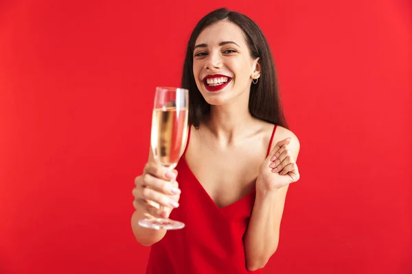 カメラを乾杯グラス シャンパン 赤の背景に分離を保持のドレスで陽気な若い女性の肖像画 — ストック写真