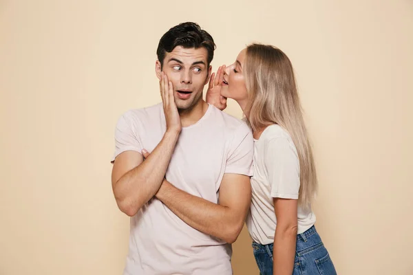 Retrato Jovem Casal Surpreso Juntos Sobre Fundo Bege Contando Segredos — Fotografia de Stock