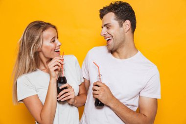 Mutlu genç çift birbirine bakarak bir cam şişe gazlı içecek içme sarı zemin üzerinde izole ayakta