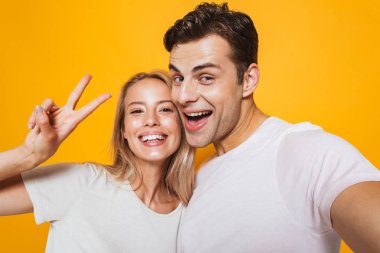 Kamera tarafından barış hareketi gösteren bir selfie almak mutlu heyecanlı genç seven Çift sarı duvar arka plan üzerinde izole ayakta fotoğraf.