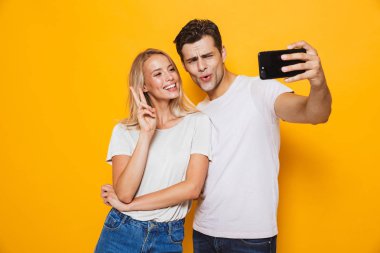 Fotoğraf mutlu seven Çift sarı duvar arka plan üzerinde izole duran genç bir selfie cep telefonuyla almak heyecanlı olun barış hareketi.
