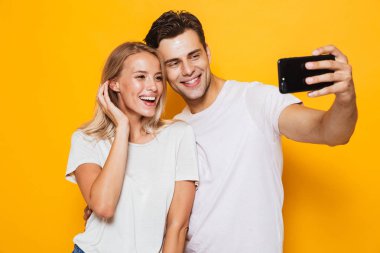 Mutlu heyecanlı genç seven Çift sarı duvar arka plan üzerinde izole ayakta fotoğrafını çekin bir selfie cep telefonuyla.