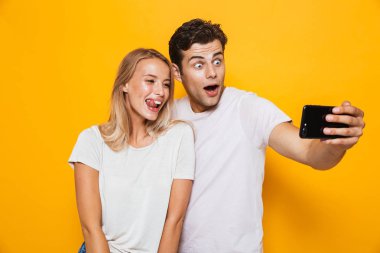 Mutlu heyecanlı genç seven Çift sarı duvar arka plan üzerinde izole ayakta fotoğrafını çekin bir selfie cep telefonuyla.