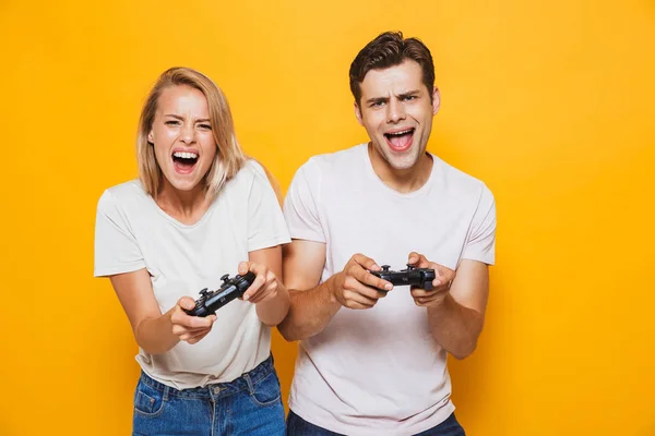 幸せな興奮若いカップルの分離に立って黄色の壁背景は ジョイスティックでゲームをプレイを愛するの写真 — ストック写真