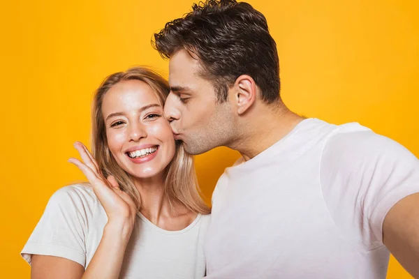 照片的快乐兴奋的年轻情侣站在黄色墙上的背景隔离自拍相机接吻 — 图库照片