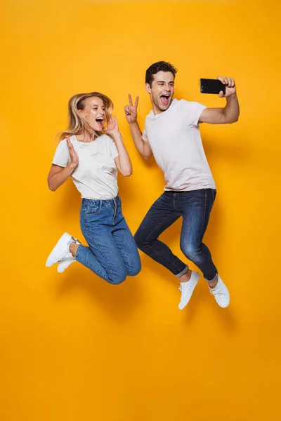黄色の壁の背景分離を飛び越えて幸せな興奮若い愛するカップルの写真は Selfie を作る — ストック写真