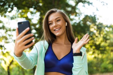 Genç ve güzel fotoğrafını cep telefonu sallayarak tarafından konuşmak kulaklık ile kadın park açık havada dinleme müzik spor.