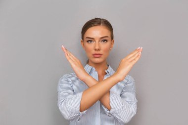Serious young businesswoman standing over gray background, showing crossed arms gesture clipart