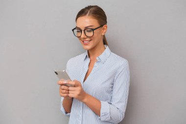 Cep telefonu kullaranarak gri duvar arka plan üzerinde duran güzel gülümseyen iş kadın görüntüsünü.
