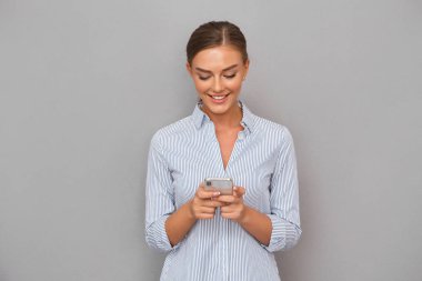Cep telefonu kullaranarak gri duvar arka plan üzerinde duran güzel gülümseyen iş kadın görüntüsünü.