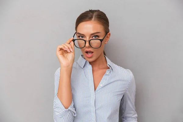 メガネをかけてグレーの壁の背景の上に立って美しいショックを受けたビジネス女性のイメージ — ストック写真