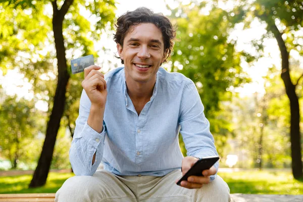 Kredi Kartı Gösteren Şehir Parkta Otururken Cep Telefonu Tutan Genç — Stok fotoğraf