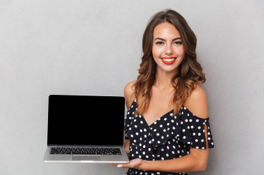 Boş ekran dizüstü bilgisayar holding neşeli bir genç kız elbise gri arka plan üzerinde portresi