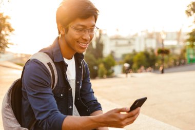 Parkta otururken smartphone kullanarak gözlük neşeli Asya erkek öğrenci