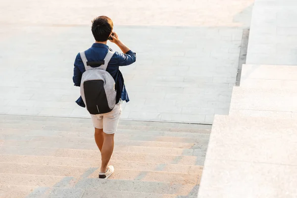 Back view of asian male student talking by smartphone while walking on stairs outdoors