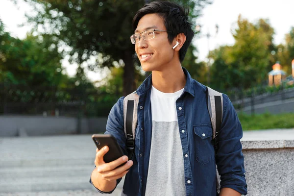 Lachende Aziatische Mannelijke Student Brillen Oortelefoons Smartphone Houden Terwijl Weg — Stockfoto