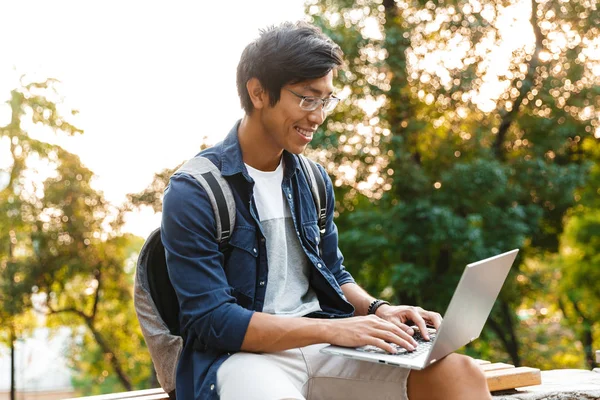 Удовлетворенный Азиатский Студент Очках Помощью Ноутбука Сидя Скамейке Парке — стоковое фото