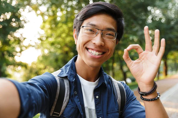 Sonriente Asiático Macho Estudiante Gafas Haciendo Selfie Mostrando Signo Mientras — Foto de Stock