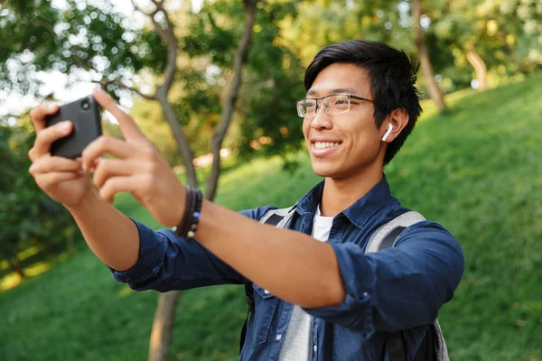 公園内でありながらスマート フォンの Selfie を作る眼鏡でアジアの男子生徒の笑顔 — ストック写真