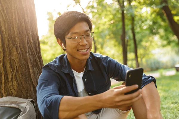 Park Ağaç Yakınındaki Otururken Smartphone Kullanarak Gözlük Mutlu Asya Erkek — Stok fotoğraf