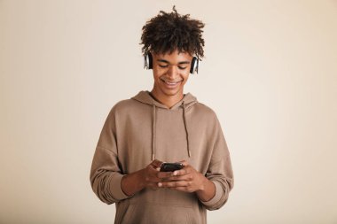 İzole, hoodie cep telefonu tutan kulaklıklarla müzik dinlerken mutlu bir genç afro Amerikalı adam portresi giymiş