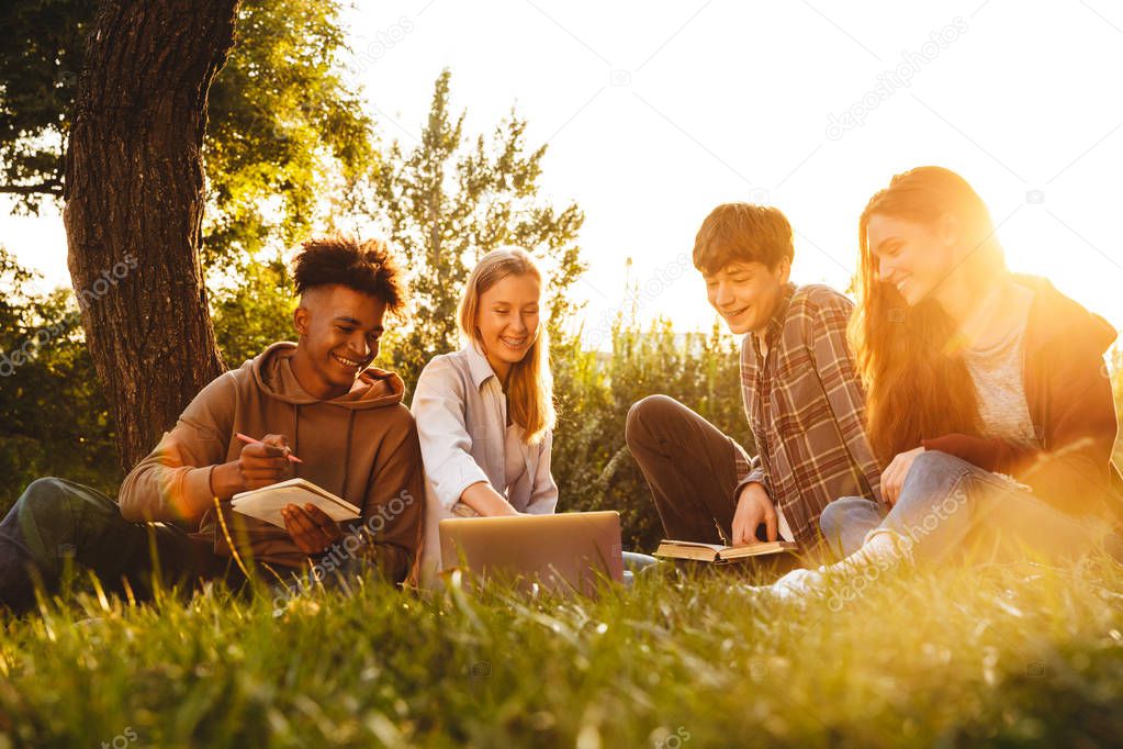 Group of positive multhiethnic students doing homework together at the park, using laptop computer