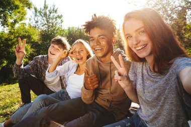 Grup birlikte sonra parkta, ödev heyecanlı multhiethnic öğrenci cep telefonu ile bir selfie alarak